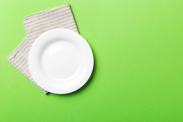 Top view on colored background empty round white plate on tablecloth for food. Empty dish on napkin with space for your design. - Foto, Imagem