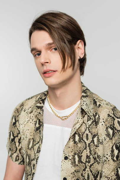 stylish bigender person in snakeskin print blouse and golden necklace looking at camera isolated on grey - Photo, image