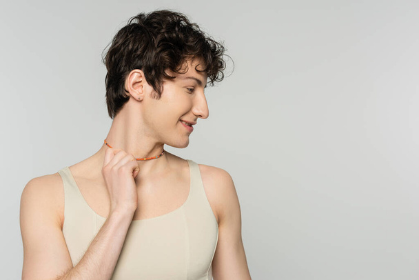 profile of curly bigender model in tank top touching colorful beads isolated on grey - Fotó, kép