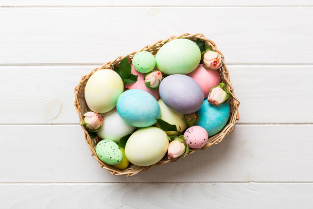 Happy Easter. Easter eggs in basket on colored table with yellow roses. Natural dyed colorful eggs background top view with copy space. - Foto, afbeelding