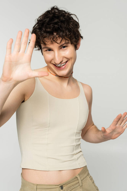 carefree pangender person in tank top gesturing and smiling at camera isolated on grey - Photo, Image