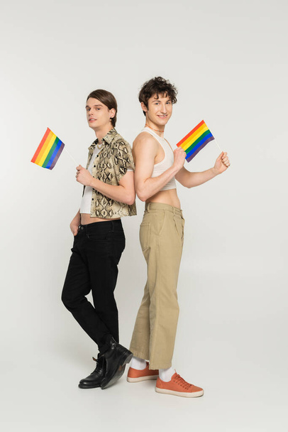 full length of stylish pansexual models posing with small lgbt flags on grey background - Photo, Image