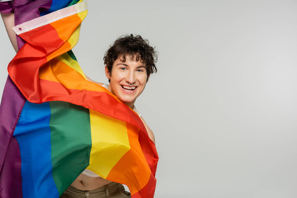 overjoyed pangender model with lgbt flag looking at camera isolated on grey - Foto, Bild
