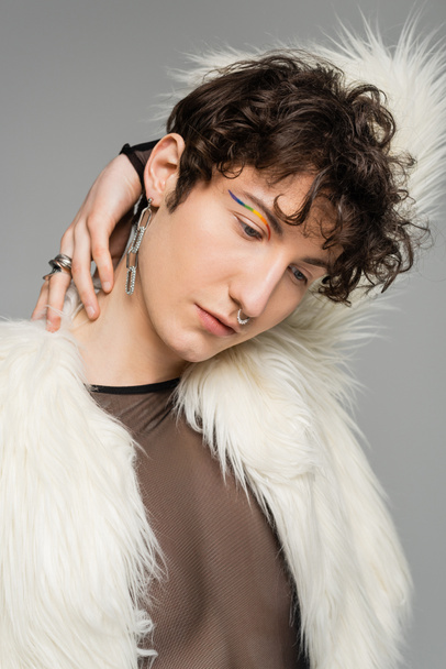 portrait of fashionable bigender person with rainbow eye liner posing in white faux fur jacket isolated on grey - Foto, Imagem