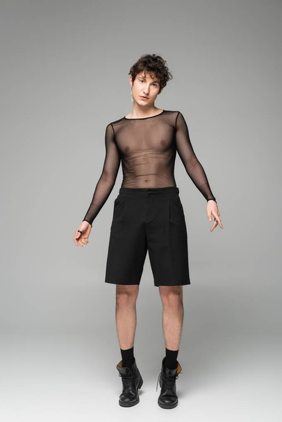 full length of nonbinary person in transparent top and black shorts on grey background - Фото, изображение