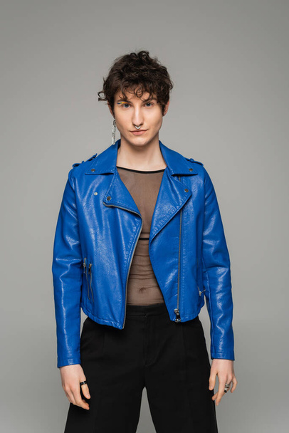 fashionable pansexual model in blue leather jacket looking at camera isolated on grey - Foto, imagen