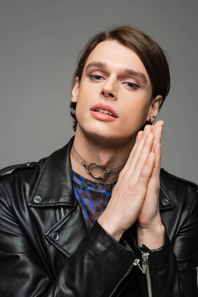 portrait of stylish pansexual person with makeup and praying hands looking at camera isolated on grey - Fotoğraf, Görsel