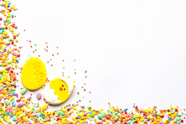 Pasen decor concept. Frame gemaakt van suikerhagelslag met een gele decoratie in de vorm van een ei en een kip op een witte achtergrond met een lege ruimte in het midden. Kopieerruimte - Foto, afbeelding