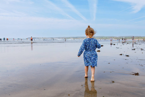 Little cute toddler girl at the Ballybunion surfer beach, having fun on with playing on west coast of Ireland. Happy child enjoying Irish summer and sunny day with family - Foto, Imagen