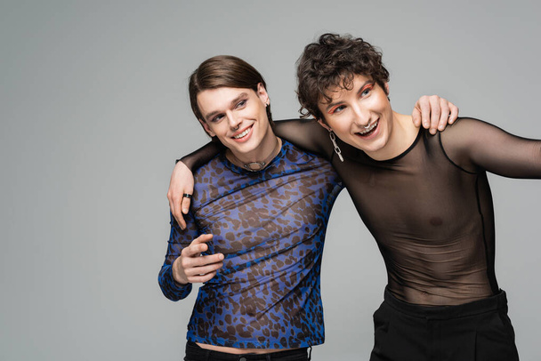 cheerful pansexual models in fashionable tops smiling and looking away isolated on grey - Valokuva, kuva