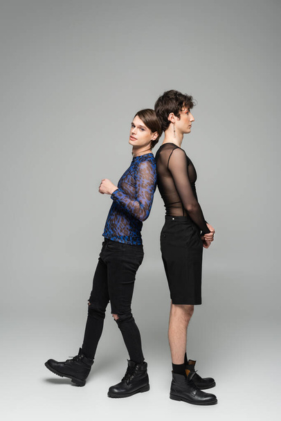 full length of pansexual partners in fashionable clothes standing back to back on grey background - Fotografie, Obrázek
