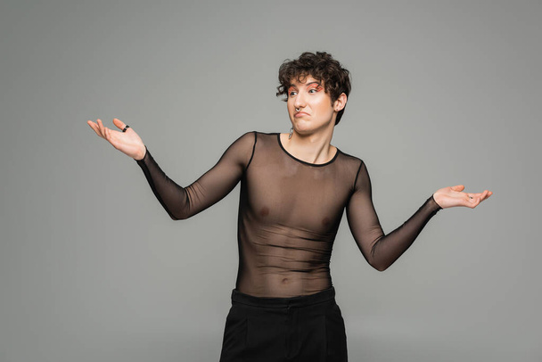 confused pangender person in black transparent top showing shrug gesture isolated on grey - Fotografie, Obrázek