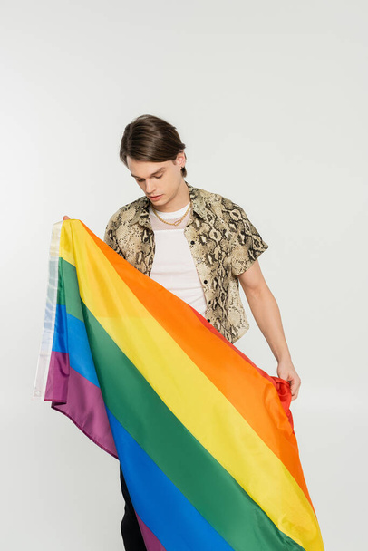 young nonbinary model in animal print blouse holding rainbow flag isolated on grey - Foto, immagini