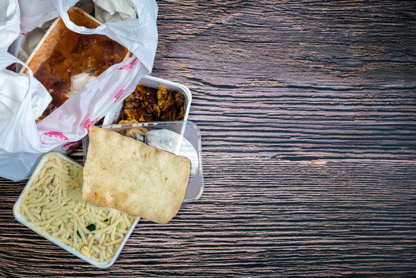 Selección de comida para llevar china en bolsa de plástico. Bami, babi pangang, carne picada crujiente, pollo agridulce, vista superior krupuk en el espacio de copia de mesa de madera. Comida a domicilio Comida rápida - Foto, Imagen