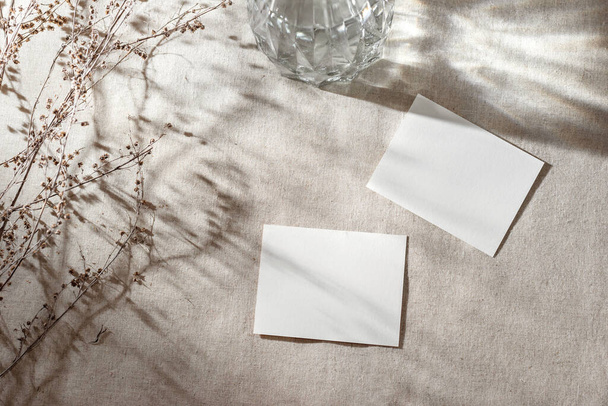 Empty paper cards with mock up copy space on a beige linen table cloth with abstract floral sunlight shadows, aesthetic business, brand, invitation template - Fotó, kép