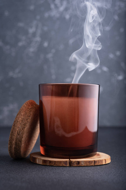 Cozy candle in brown glass jar with smoke on dark background - Fotó, kép