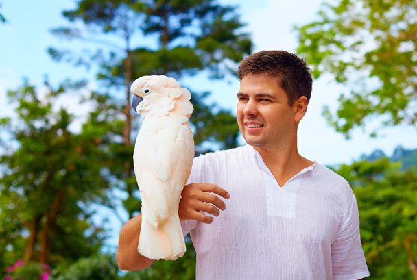 young man, ornithologist holding gorgeous cockatoo parrot - 写真・画像