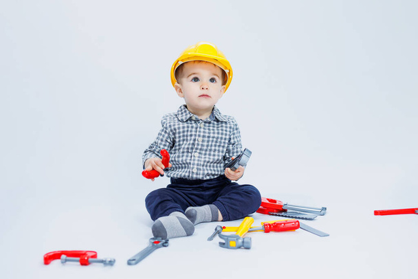 Een kleine jongen in een geruit shirt naar het beeld van een bouwer. Een jongen in een bouwhelm en plastic gereedschap - Foto, afbeelding