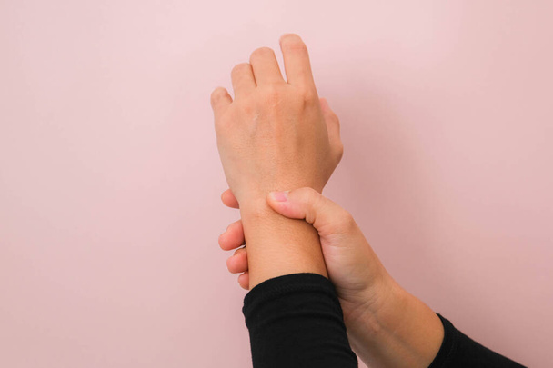 Großaufnahme der Hand einer Frau, die ihr schmerzhaftes Handgelenk von Arthritis oder Karpaltunnelsyndrom (CST) isoliert auf rosa Hintergrund hält. Gesundheitskonzept. - Foto, Bild