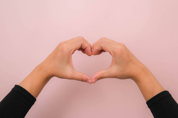 Γυναικεία χέρια που κάνουν το σύμβολο της καρδιάς απομονωμένο σε ροζ φόντο με χώρο αντίγραφο. Αγάπη έννοια για την Ημέρα του Αγίου Βαλεντίνου. - Φωτογραφία, εικόνα