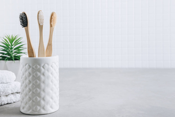 Eco toothbrushes. Bamboo toothbrushes cup, white towels on gray stone background, copy space. Minimal bath background - Photo, image