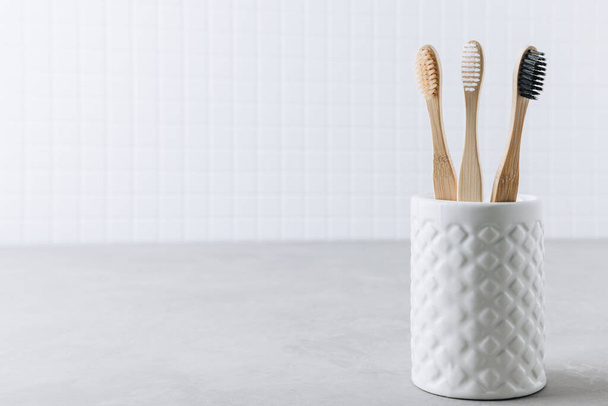 Cepillos de dientes ecológicos. Cepillos de dientes de bambú taza sobre fondo de piedra gris, espacio de copia. Fondo de baño mínimo - Foto, Imagen