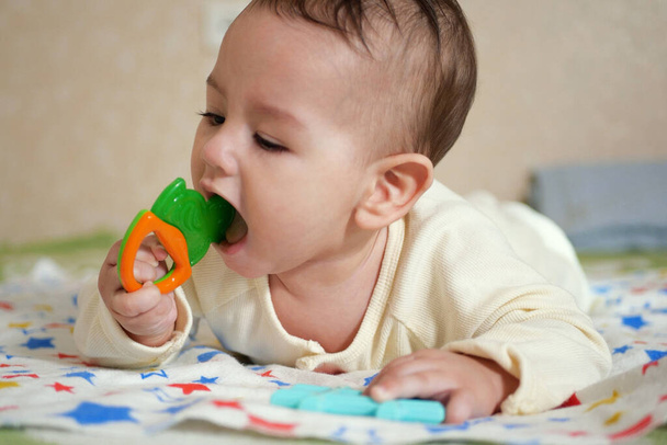 Niedliche entzückende Neugeborenes spielt mit bunten Rasselspielzeug. Baby mit Beißring. sechs Monate altes hübsches Babyporträt auf Weiß mit Beißspielzeug. - Foto, Bild