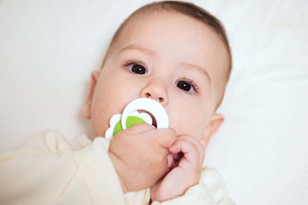 Baby sucking Pacifier looking on bed. portrait of cute newborn baby lying on bed with pacifier on mouth. - Photo, Image