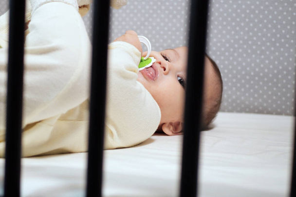 Дитина смокче Псіфер, дивлячись на ліжко. портрет милої новонародженої дитини, що лежить на ліжку з пацифістом на роті
. - Фото, зображення