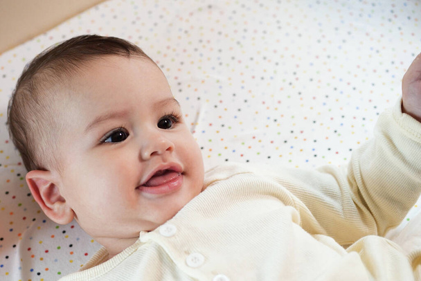 Ευτυχισμένο νεογέννητο μωρό κάνει ένα αστείο πρόσωπο. Πορτραίτο ενός μωρού που σέρνεται στο δωμάτιό του από κοντά. - Φωτογραφία, εικόνα