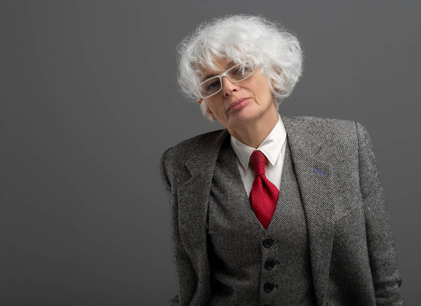élégante élégante femme âgée aux cheveux blancs dans des lunettes et costume formel conservateur bien adapté posant avec une expression confiante et composée montrant l'expérience professionnelle et l'accessibilité  - Photo, image