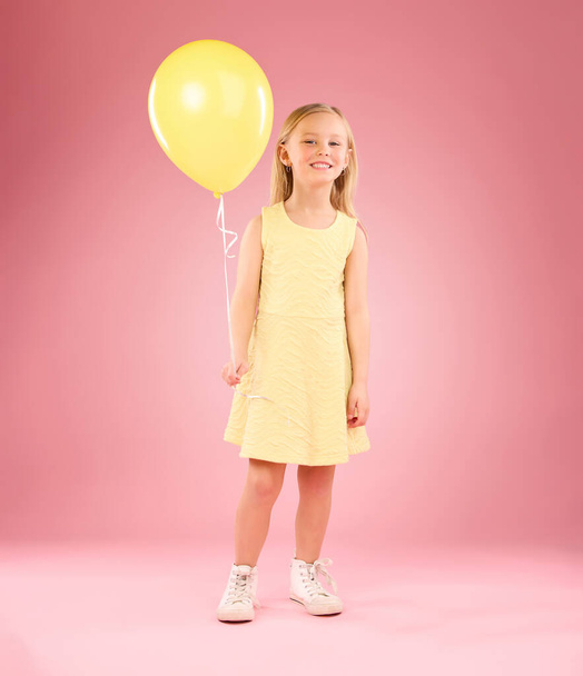Girl, child and portrait with a balloon in studio on a pink background with smile. Female kid model with happiness, creativity and yellow birthday party decoration in hand isolated on color and space. - Photo, Image
