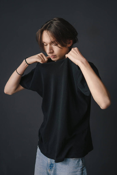Young man wanting to pull his black t-shirt over his head, undresses. Black studio. - Photo, Image