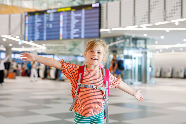 Little preschool girl at airport terminal. Happy child going on vacations by airplane. Smiling kid with passport and bag - Photo, Image