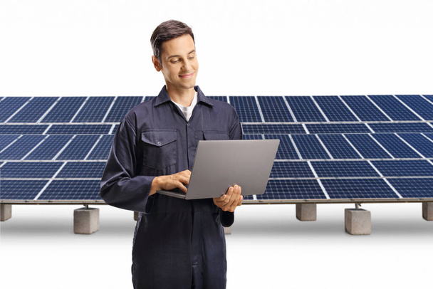 Young male worker in a uniform working with a laptop computer on a solar farm isolated on white background - Foto, Bild