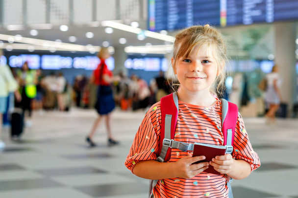 Little preschool girl at airport terminal. Happy child going on vacations by airplane. Smiling kid with passport and bag - Fotó, kép