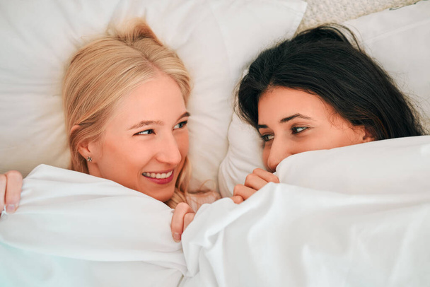Love, above and lesbian couple in bed, waking up and bonding in their home together. Lgbt, gay and happy women sharing romance, relationship and sweet moment in a bedroom, in love and content. - Фото, изображение