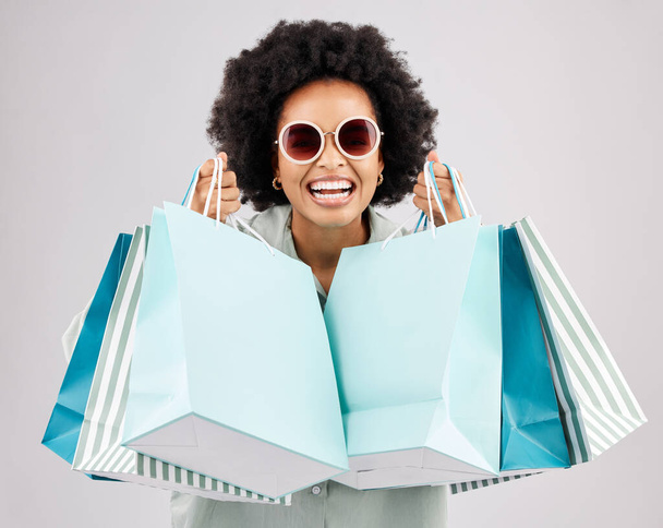 Portrait, sacs à provisions et femme noire riant avec des lunettes de soleil en studio isolé sur fond blanc. Offres de vente, la mode et le bonheur d'une personne riche, drôle et riche avec des produits de détail - Photo, image