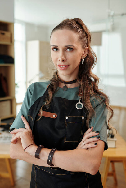 Portrait of smiling leather worker in denim apron crossing arms and looking at camera - Fotoğraf, Görsel