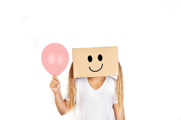 Woman with her head in a box  happiness gesture drawn on it and holding a pink balloon standing on a white background with copy space - Photo, Image