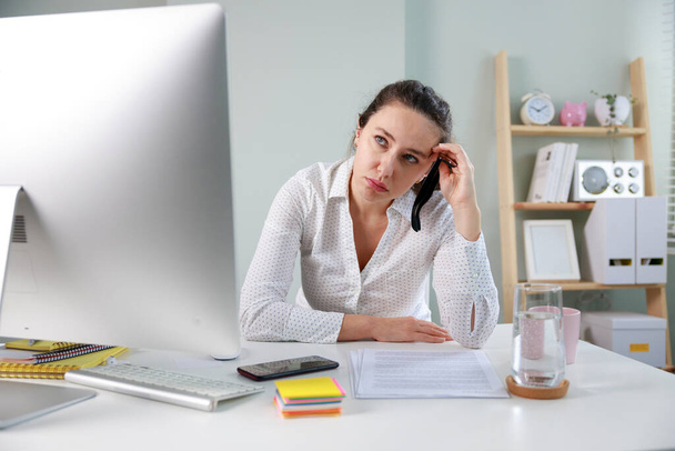 Serious freelancer worker with eyeglasses and in white shirt sitting in home office, holding her hea - Foto, imagen