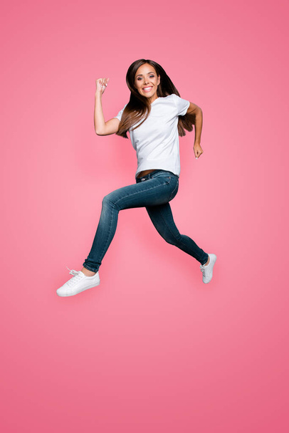 Full lenght portrait of brown-haired gorgeous attractive nice lovely excited smiling young lady wearing jeans and white t-shirt, flying showing motion running hurry over grey background, isolated. - Foto, afbeelding