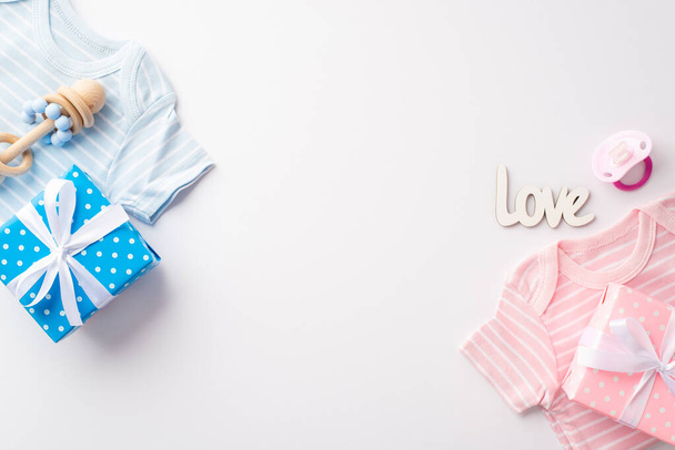Le genre révèle le concept du parti. Vue du dessus photo de rose et bleu vêtements pour bébés chemises boîtes cadeaux sucette hochet en bois et inscription amour sur fond blanc isolé avec copyspace - Photo, image