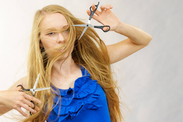 Haircut coiffure haircare concept. Girl with blowing long blond hair holding scissors, showing work tools, normal and thinning shears. - Photo, Image