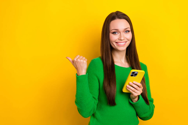 Portrait of pretty positive lady hold smart phone direct finger empty space isolated on yellow color background. - Foto, immagini