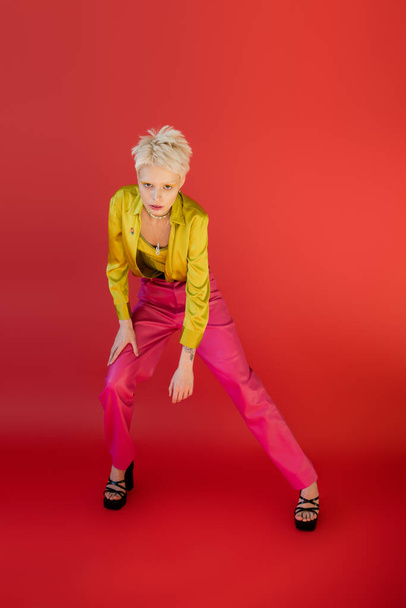 full length of young albino model in trendy outfit posing on carmine pink  - Foto, immagini