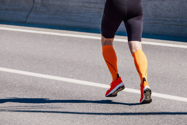 piernas corredor masculino en calcetines de compresión naranja y medias negras corren carrera en la carretera, competición deportiva de resistencia - Foto, imagen