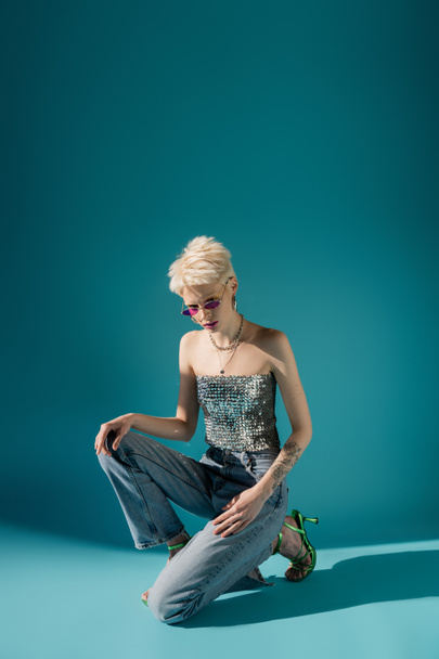teljes hossza tetovált albínó modell trendi napszemüveg és ruha pózol a kék háttér  - Fotó, kép