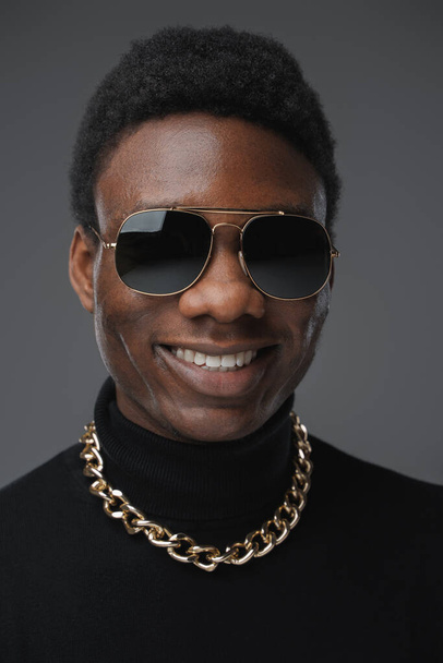 Trendy african man with turtleneck sweater and sunglasses. High quality photoStudio shot of stylish black guy dressed in sweater and sunglasses with golden chain. - Photo, Image