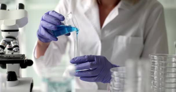 Científico sostiene en mano frasco de laboratorio vierte líquido tóxico azul. Experimentos químicos e investigación de laboratorio - Imágenes, Vídeo